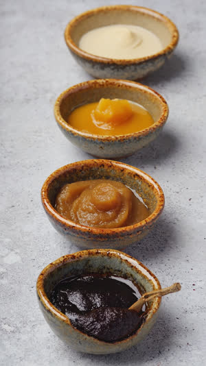 Two small ceramic dishes side by side, one holding pale ivory miso and one holding near-black soybean miso, stark tonal contrast, flat lay, even soft light