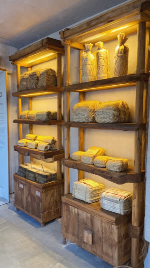 Rows of straw-wrapped natto bundles displayed on a shop counter, handmade straw ties, warm shop lighting, traditional Japanese retail atmosphere