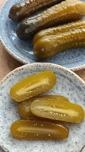 Sliced nukazuke pickles arranged on a small ceramic plate, deep olive and amber tones, glistening moist cut surfaces, close-up, clean natural light