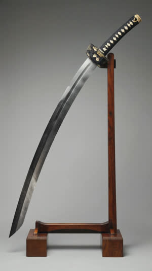 A Japanese katana blade resting horizontally on a simple two-prong wooden display rack, soft even museum lighting, a misty white hamon temper line visible along the cutting edge,…