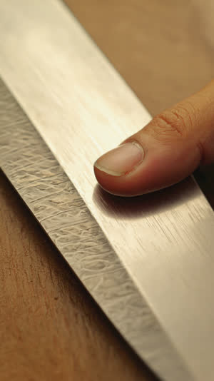 Extreme close-up of a fingertip pressing a tiny finishing stone sliver against a sword surface, delicate precise motion, shallow depth of field, warm craft light
