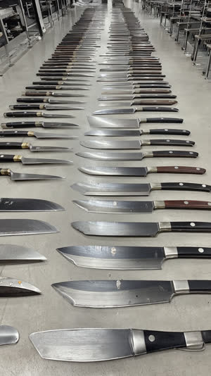 Overhead view of rows of finished Japanese blades, kitchen knives and scissors arranged in precise lines, factory finishing room, clean industrial light