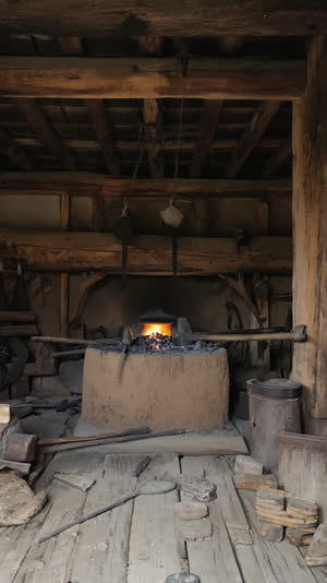 Old Japanese swordsmith forge interior, clay furnace, hammers and tongs on dark wood, centuries-old timber beams, soft ember glow, historical atmosphere