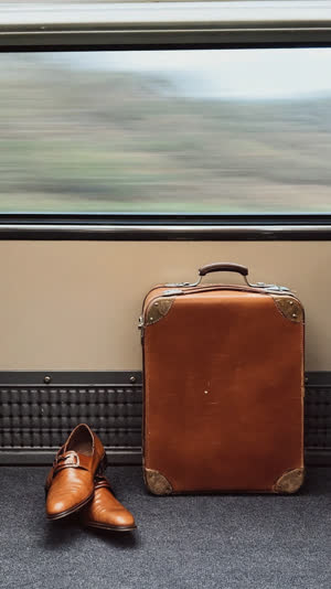 Traveler's suitcase and shoes standing in a calm train aisle, scenery streaming past the window behind, soft focus