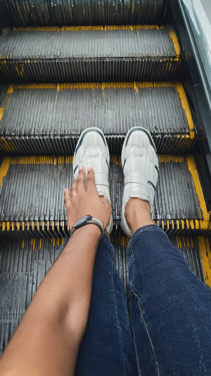 Hand resting on an escalator handrail with feet planted together on one step, calm confident stance, soft station light