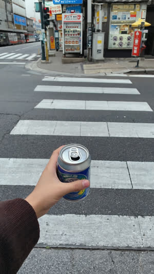 Hand holding an empty drink can on a clean Japanese street corner with no trash can anywhere, puzzled pause implied, daylight
