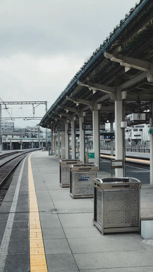 Station front where planters and signboards stand in place of old bins, quiet urban continuity, soft overcast light