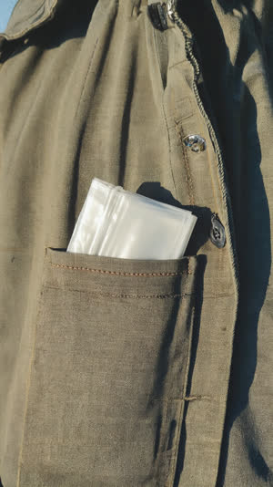 Folded small plastic bag peeking from a traveler's jacket pocket, simple practical detail, soft daylight