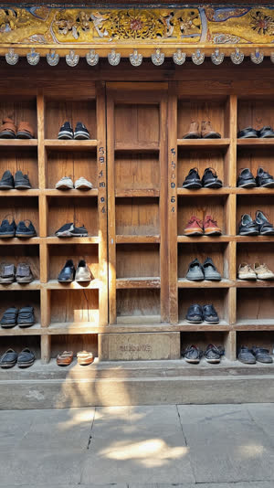 Wooden shoe shelves at a temple entrance filled with visitors' shoes, numbered slots, aged wood, dappled daylight through the doorway