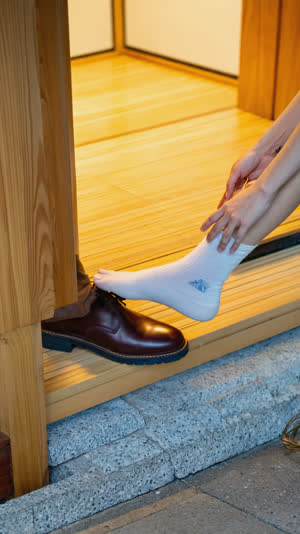Side view of feet slipping out of shoes at a ryokan step, one sock foot rising to the wooden ledge, warm light, feet and