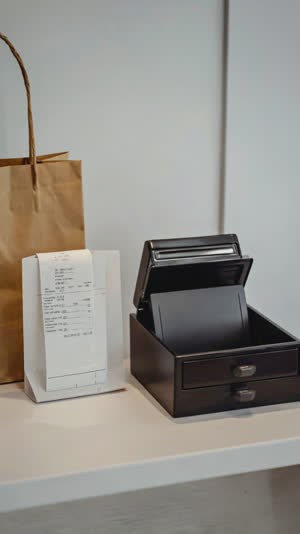 Tidy shop counter after a purchase, empty cash tray at rest, receipt roll and folded bag nearby, calm still-life order, soft light
