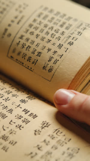 Aged Japanese dictionary pages under warm light, delicate thin paper and dense type, a fingertip at the page edge, close-up