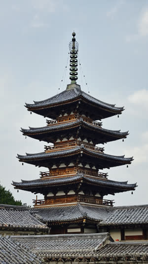 Looking up at the stacked tiled roofs of a five-story Japanese wooden pagoda against the sky, layered eaves, photorealistic documentary photograph, natural soft light, muted…
