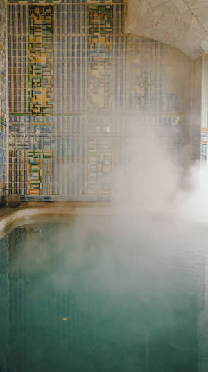 Steamy interior of a Japanese sento bath hall, colorful tile mosaic wall, rising steam over clear hot water, soft diffused light, serene atmosphere