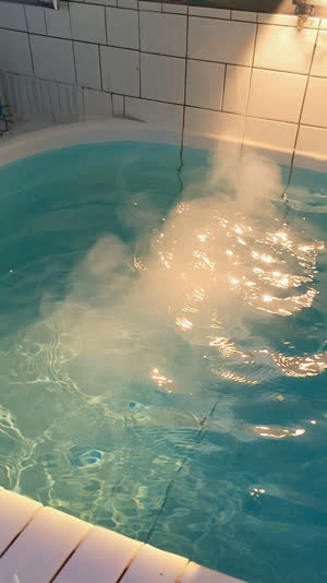 Overhead close-up of gently rippling hot bathwater in a tiled sento tub, steam rising, warm light reflections on water surface, tranquil mood