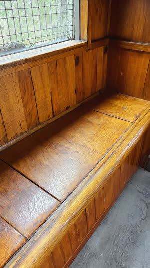 Close-up of a bandai booth's worn wooden seat and rail, decades of polish and patina on wood grain, soft window light, tactile nostalgic detail