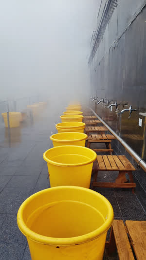 Long row of yellow bath buckets receding into distance at sento washing stations, telephoto compression, rhythmic repetition, steamy atmosphere