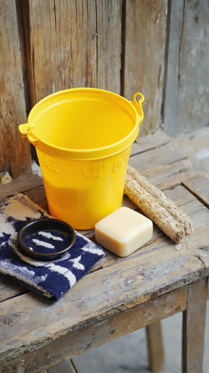 Flat lay of Japanese bath set, yellow bucket, folded tenugui towel, bar of soap, arranged on wooden bench, warm nostalgic still life