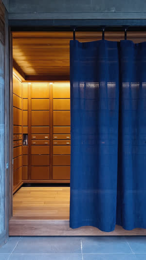 Low angle view under a split noren curtain revealing bathhouse entryway beyond, shoe lockers glowing warmly inside, point-of-view of entering