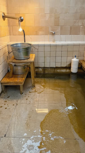 Washing station with bucket and stool returned neatly in place, orderly tiles glistening, quiet after-use tidiness, warm ambient light