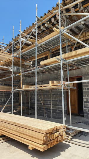 Construction scaffolding and fresh lumber against a traditional bathhouse building under renovation, old and new materials side by side, hopeful daylight