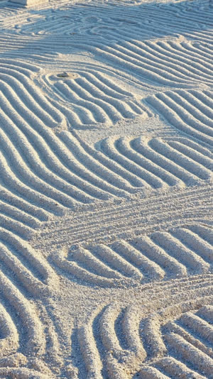 Close-up of raked white gravel with wave-like parallel ridges in a Japanese dry garden, low side light casting shadows in the grooves, photorealistic documentary photograph,…