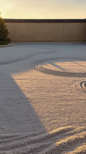 Low evening light raking across a Zen garden's earthen wall and gravel, long soft shadows, silent austere mood, photorealistic documentary photograph, natural soft light, muted…