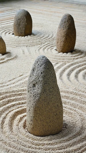 Several distinct natural weathered garden stones of different shapes standing and reclining in raked gravel, each with its own posture and character, natural irregular weathered…