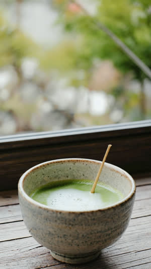 A ceramic bowl of freshly whisked matcha tea with delicate green foam in the foreground, a luminous Japanese garden blurred beyond, closing contemplative mood, whisked liquid tea…