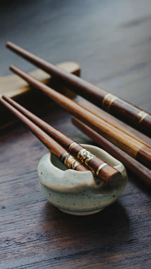 Close-up of lacquered chopsticks resting on a ceramic hashioki, wood grain and lacquer sheen, dark table, quiet minimal composition