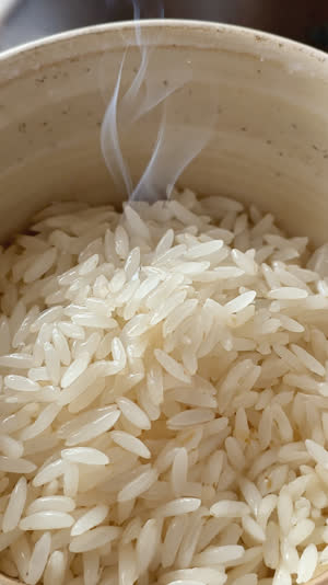 Overhead macro of freshly steamed white rice in a ceramic bowl, glossy grains, faint steam rising, warm soft light