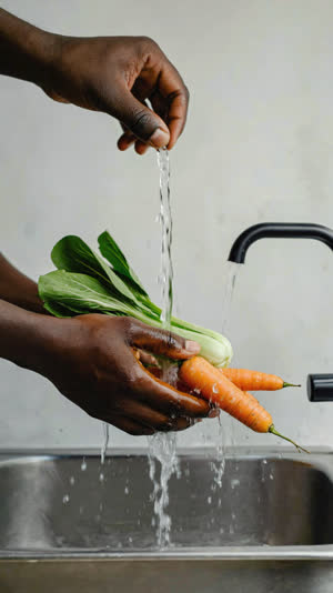 Hands washing fresh vegetables under running water in a Japanese kitchen, droplets caught in light, close crop on