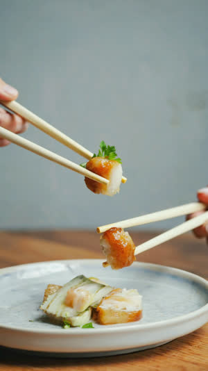 Two pairs of chopsticks reaching toward the same morsel above a plate at frame edges, suspended tense moment, soft light