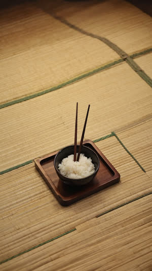 A small tray holding one bowl of rice with chopsticks standing upright, dim tatami room, hushed ceremonial mood, muted tones