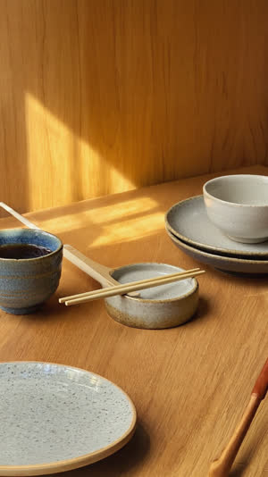 Warm dining table with chopsticks properly resting on a hashioki before a Japanese meal, gentle golden light, calm relieved mood