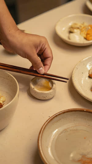 A hand gently placing chopsticks onto a small ceramic rest mid-meal, close-up on hands and table, soft warm light