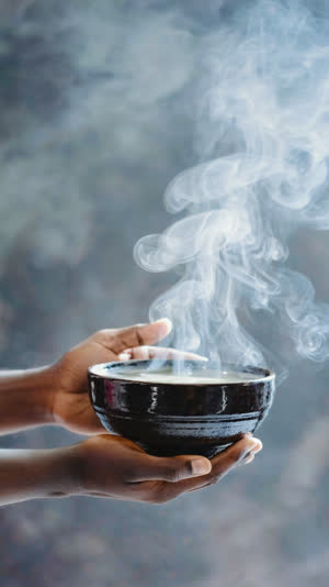 Lacquered miso soup bowl raised by two hands toward the top of frame, steam curling, deep glossy lacquer, face out of frame