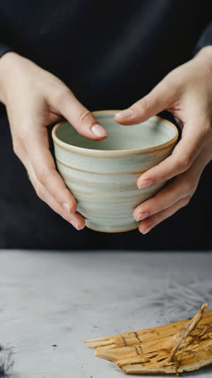 Macro of fingers supporting the footed base of a small ceramic rice bowl, correct Japanese grip, delicate porcelain texture, soft light