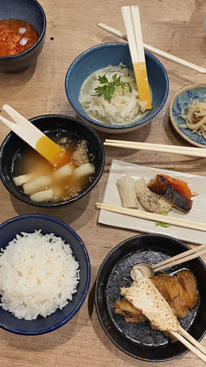Overhead of a casual Japanese meal with paper-sleeved disposable chopsticks laid across, everyday diner atmosphere, warm light
