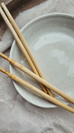 Used disposable chopsticks resting on an emptied dish, quiet aftermath still life, muted tones, contemplative light