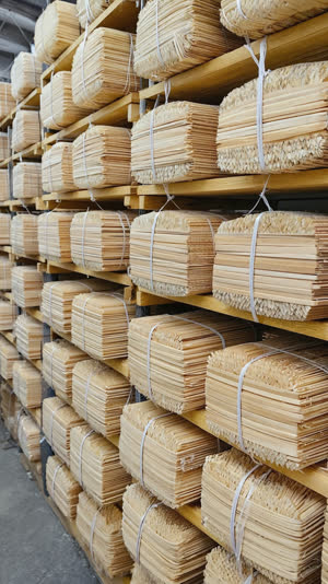 Stacked bundles of finished disposable chopsticks in a Yoshino, Nara workshop, shelves of pale cedar bundles, industrious warm atmosphere