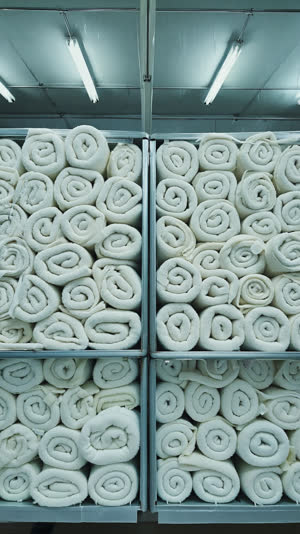 Hundreds of identical rolled white towels lined in neat rows in stacked crates, industrial laundry facility, repeating pattern, cool clean light