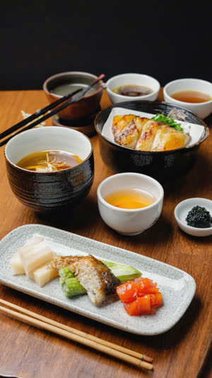 Angled overhead of a full Japanese meal set, main dish back-right, side dishes back-left, pickles in the center, every bowl in its assigned position, warm light