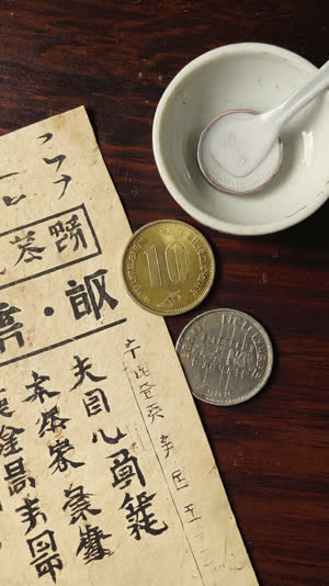 Japanese handwritten bill slip with a few hundred-yen coins beside a small empty appetizer bowl, close-up on paper texture and coins, warm light