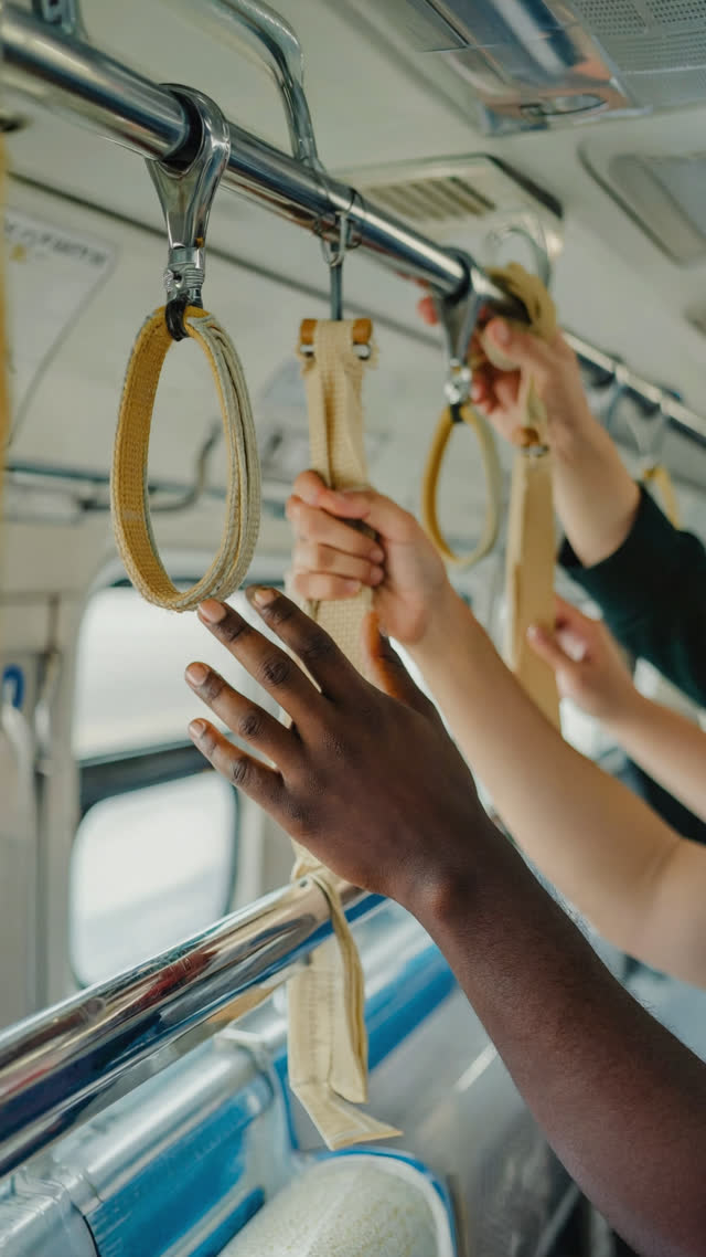 Close-up of hands sharing a train handrail and straps inside a crowded Japanese train car, warm human detail without faces, shallow depth of field
