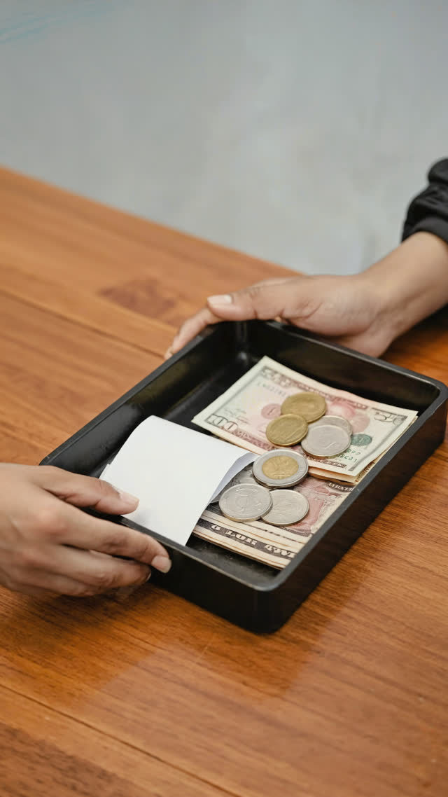 Change and receipt returned on a small tray, one hand steadying the tray edge, gentle motion, warm counter light