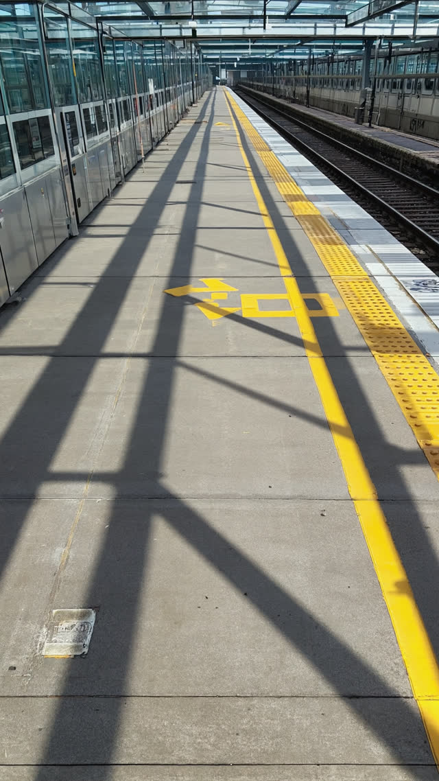 Empty train platform moments after departure, painted queue lines remaining in perfect order, long shadows, quiet atmosphere