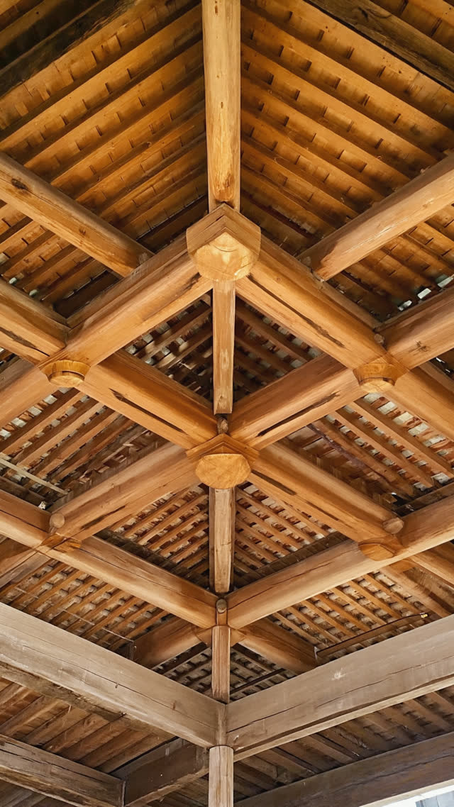 Upward view into a lattice of interlocking wooden beams forming a temple ceiling structure, geometric repetition, warm dim light, photorealistic documentary photograph, natural…