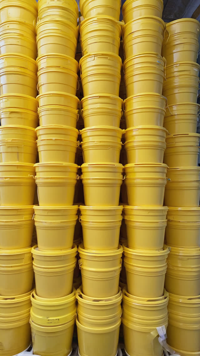 Tall stacks of identical yellow bath buckets in neat rows, repetition and mass-production feel, clean graphic composition, bright even lighting