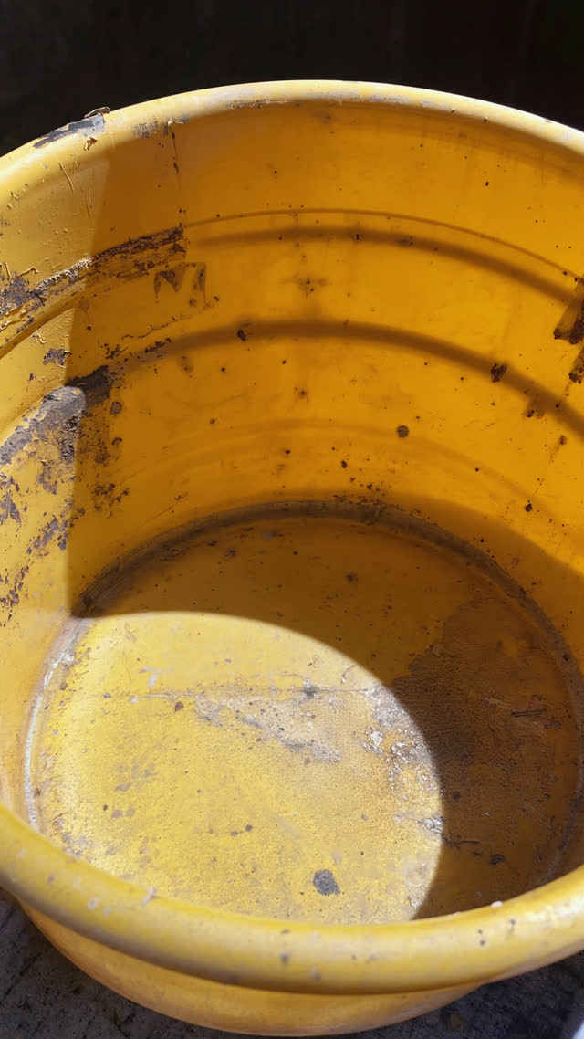 Macro shot of a decades-old yellow bath bucket with worn scratched edges, battle scars of long use, raking light on scuffed plastic texture